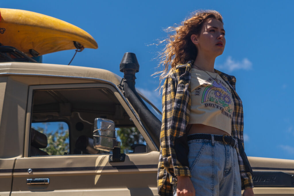 Garota de cabelo cacheado em frente a um carro olhando para o horizonte na série Selenkay