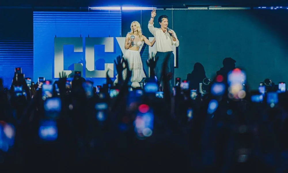 Anya Taylor-Joy à esquerda, e Miles Teller, à direita, ambos no centro do palco sendo ovacionados por uma plateia no Palco Thunder da CCXP24, sábado, para anunciar "Entre Montanhas", da Apple TV+