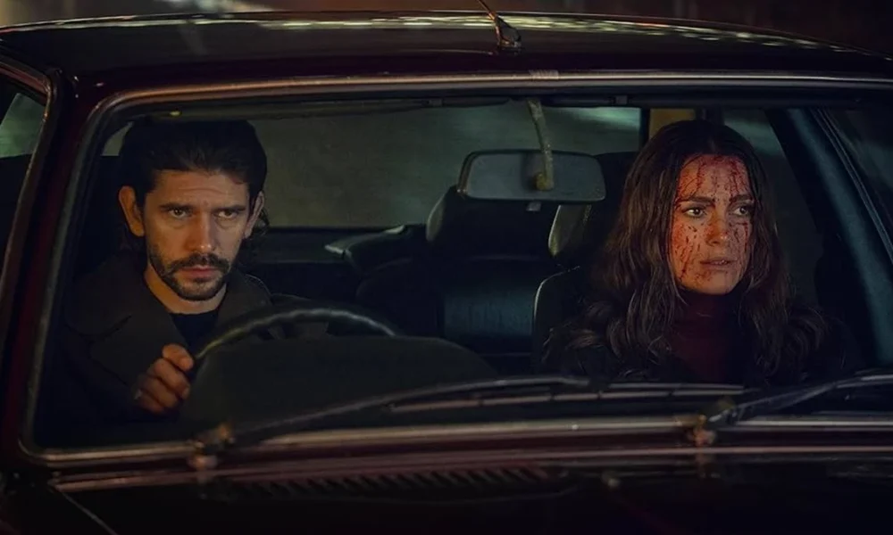 Protagonistas de Black Doves, pela Netflix. Eles estão em um carro, com o protagonista dirigindo e a protagonista com o rosto cheio de sangue.