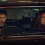 Protagonistas de Black Doves, pela Netflix. Eles estão em um carro, com o protagonista dirigindo e a protagonista com o rosto cheio de sangue.