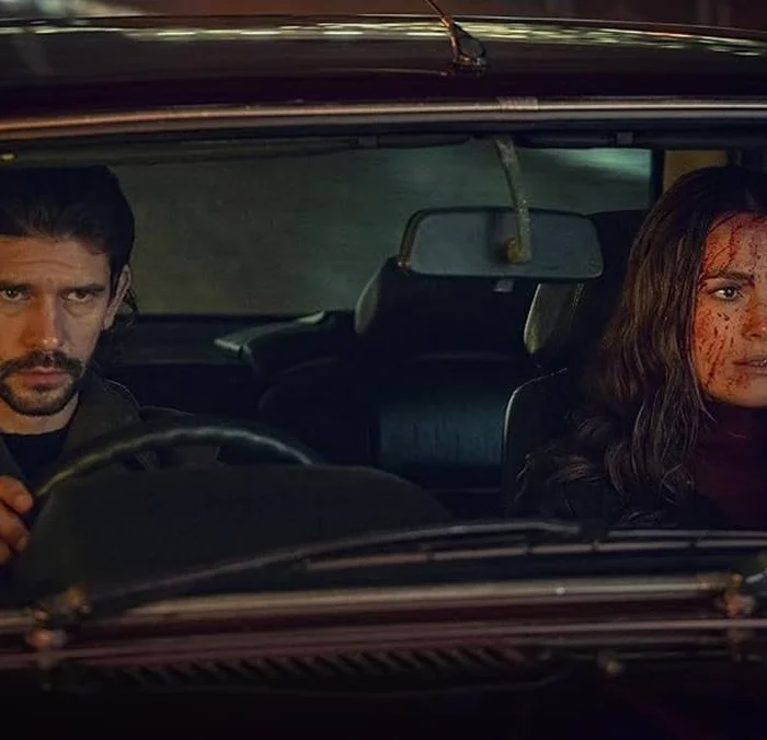 Protagonistas de Black Doves, pela Netflix. Eles estão em um carro, com o protagonista dirigindo e a protagonista com o rosto cheio de sangue.