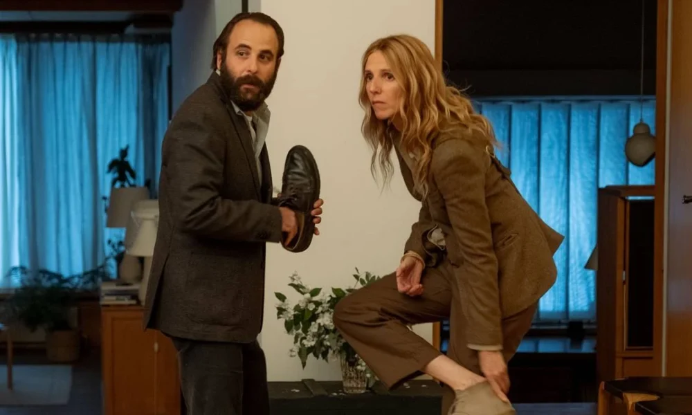 Os protagonitas de "Crônica de uma Relação Passageira" (2022) tirando os sapatos dentro de uma casa.