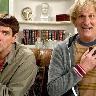 Debi e Lóide, protagonistas de filme homônimo, sentados em um sofá. Há uma estante atrás deles.