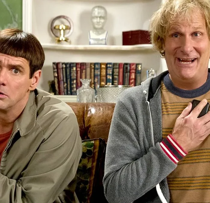 Debi e Lóide, protagonistas de filme homônimo, sentados em um sofá. Há uma estante atrás deles.