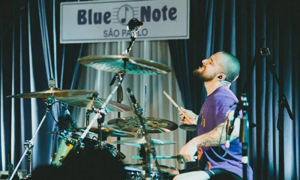 Baterista Eloy Casagrande no espaço Blue Note, em São Paulo, tocando bateria. Eloy está na segunda metade da tela, rosto inclinado para cima, enquadrado de perfil.