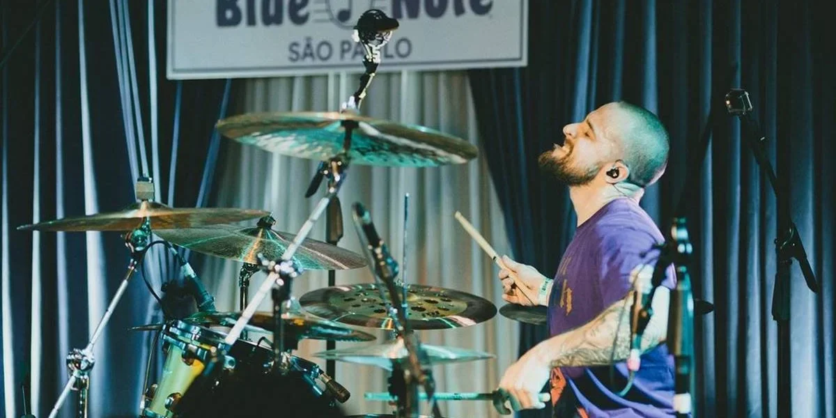 Baterista Eloy Casagrande no espaço Blue Note, em São Paulo, tocando bateria. Eloy está na segunda metade da tela, rosto inclinado para cima, enquadrado de perfil.