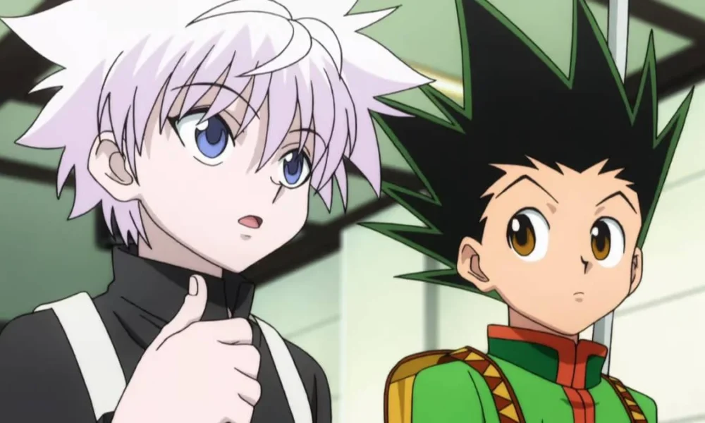 Killua Zoldyck e Gon Freecss, da esquerda para a direita, do anime Hunter x Hunter. Killua olha para um outro personagem à direita da câmera, enquanto Gon olha para Killua falando.