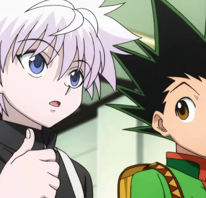 Killua Zoldyck e Gon Freecss, da esquerda para a direita, do anime Hunter x Hunter. Killua olha para um outro personagem à direita da câmera, enquanto Gon olha para Killua falando.