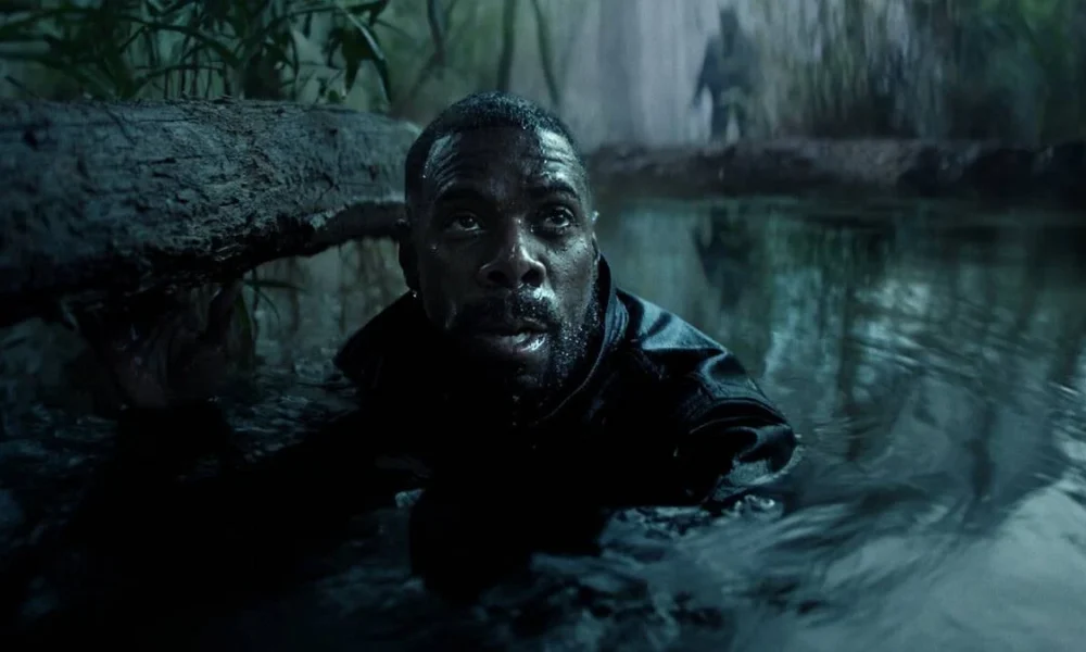 Jesse L. Martin interpretando Alec Baker, protagonista de Irracional. Personagem está com o corpo submerso até o pescoço em um aparente lago. Uma figura sombria, embaçada, está atrás dele, na margem.