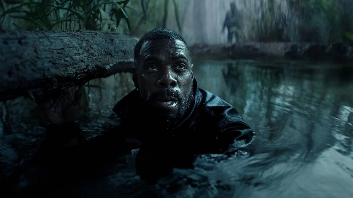 Irracional | Suspense, Paranoia e Bilionários Suspeitos nos Estados Unidos 1 Jesse L. Martin interpretando Alec Baker, protagonista de Irracional. Personagem está com o corpo submerso até o pescoço em um aparente lago. Uma figura sombria, embaçada, está atrás dele, na margem.