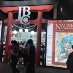 A Panini na CCXP24 | Fazendo Presença com Diverso Acervo Público visitando o estande da Editora JBC, cheio, na CCXP24. Há um torii vermelho, portal tradicional japonês, com o logo da marca, na entrada.