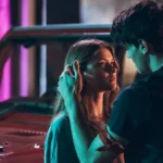 Captura de tela promocional dos protagonistas de "Sua Culpa" no filme anterior: "Minha Culpa", pela Prime Video. Imagem com luzes neon e os protagonistas se olhando, e acariciando, em frente a um carro.