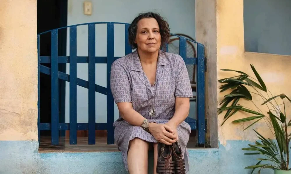 A personagem Moema (Ana Beatriz Nogueira) na novela "Mania de Você", da TV Globo. Ela está sentada no portão de uma casa, com as mãos sobre o colo.