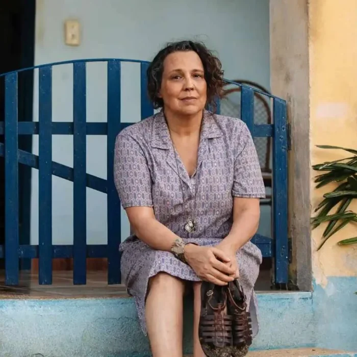 A personagem Moema (Ana Beatriz Nogueira) na novela "Mania de Você", da TV Globo. Ela está sentada no portão de uma casa, com as mãos sobre o colo.