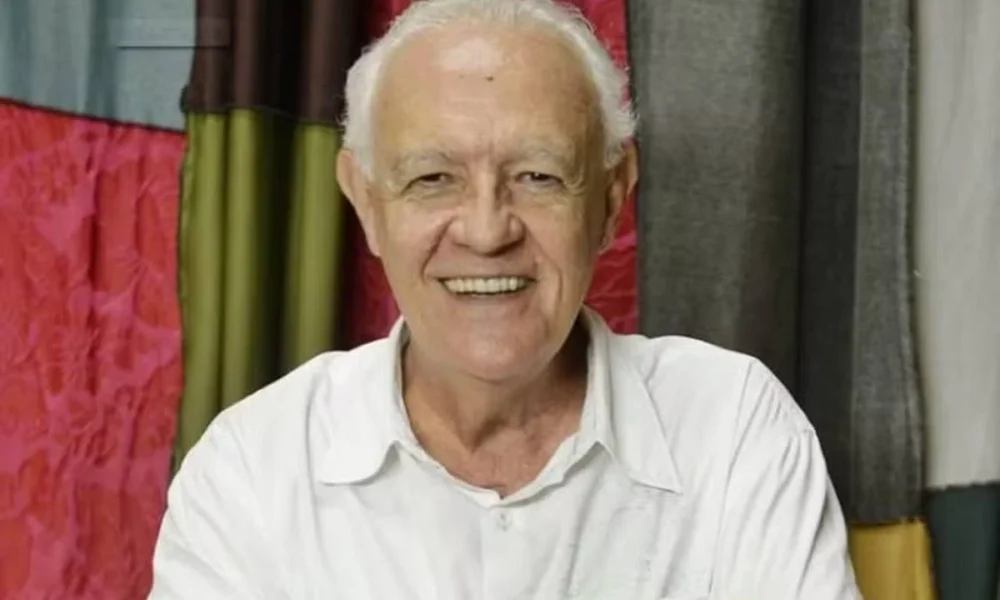 Fotografia frontal com ator Ney Latorraca sorrindo para a câmera, vestido todo de branco, já idoso.