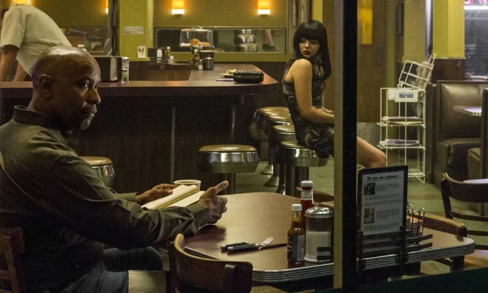 Denzel Washington como o protagonista da trilogia "O Protetor", em seu primeiro filme, de 2014, sentado em um bar lendo.