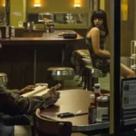 Denzel Washington como o protagonista da trilogia "O Protetor", em seu primeiro filme, de 2014, sentado em um bar lendo.