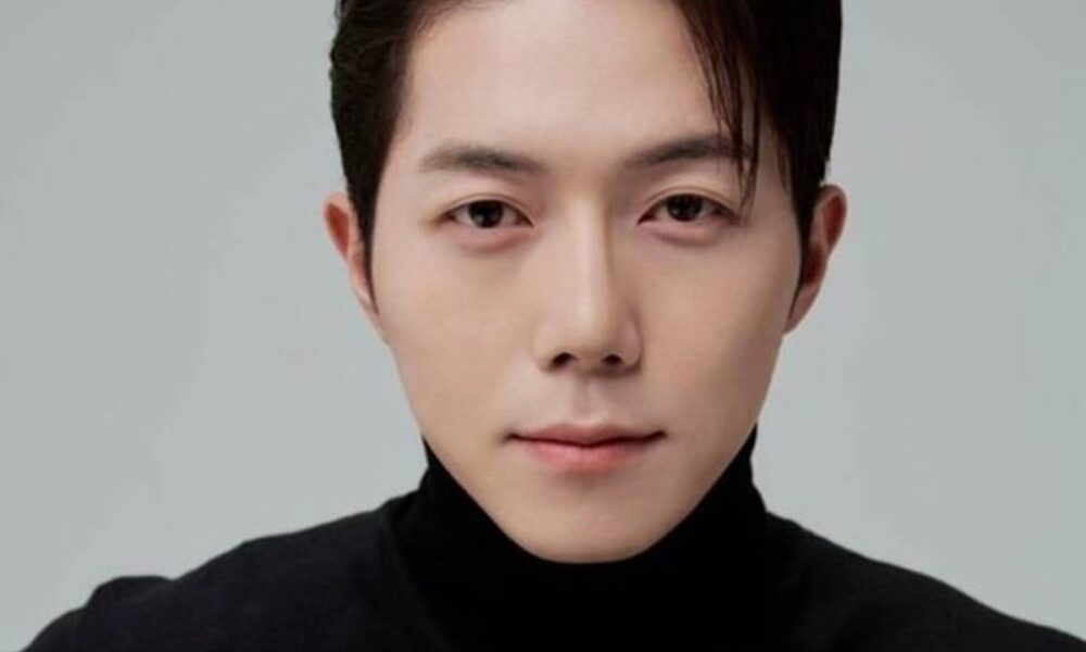 Fotografia do ator Park Min-jae, do busto para cima, olhando para a câmera. Park está com um sorriso sério e vestido de preto.