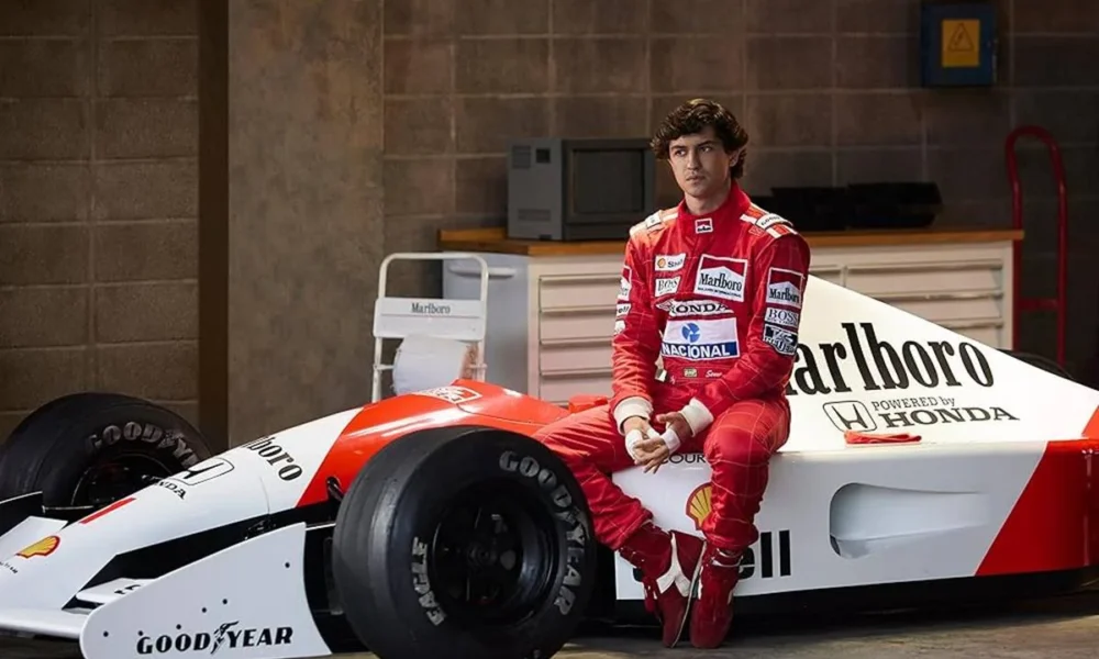 Captura de tela de divulgação da série "Senna", pela Netflix, com a história do piloto brasileiro. Senna está sentado em um carro, uniformizado.