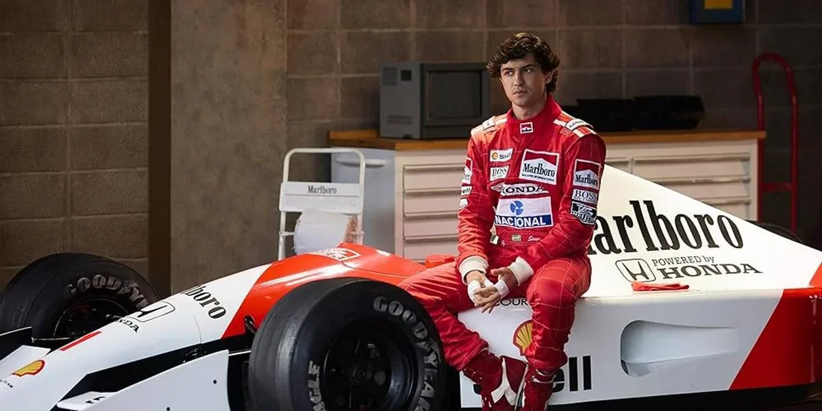 Captura de tela de divulgação da série "Senna", pela Netflix, com a história do piloto brasileiro. Senna está sentado em um carro, uniformizado.