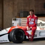 O Dia do Chacal | Eddie Redmayne Revela Surpresas e Desafios da Série que Reinventa um Clássico Captura de tela de divulgação da série "Senna", pela Netflix, com a história do piloto brasileiro. Senna está sentado em um carro, uniformizado.