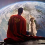 Imagem promocional para o filme "Superman" (2025), de James Gunn. O homem de aço e seu cão, Krypto, estão de costas para nós, sentados na Lua, e olhando para a Terra. Superman está com seu icônico visual azul com a longa capa vermelha e símbolo "S" marcado em amarelo na capa.
