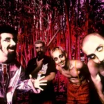 Imagem de divulgação dos 26 anos da banda System of a Down, com uma foto, em paleta vermelha, dos integrantes à época do debut.