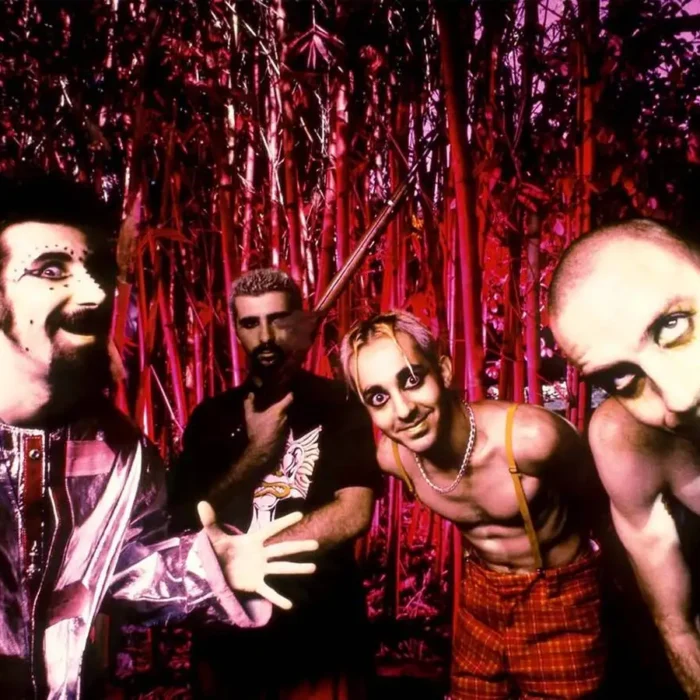 Imagem de divulgação dos 26 anos da banda System of a Down, com uma foto, em paleta vermelha, dos integrantes à época do debut.