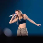 Taylor Swift em concerto em março de 2023. Cantora está com a cabeça inclinada e o microfone próximo a boca, cantando de olhos fechados.