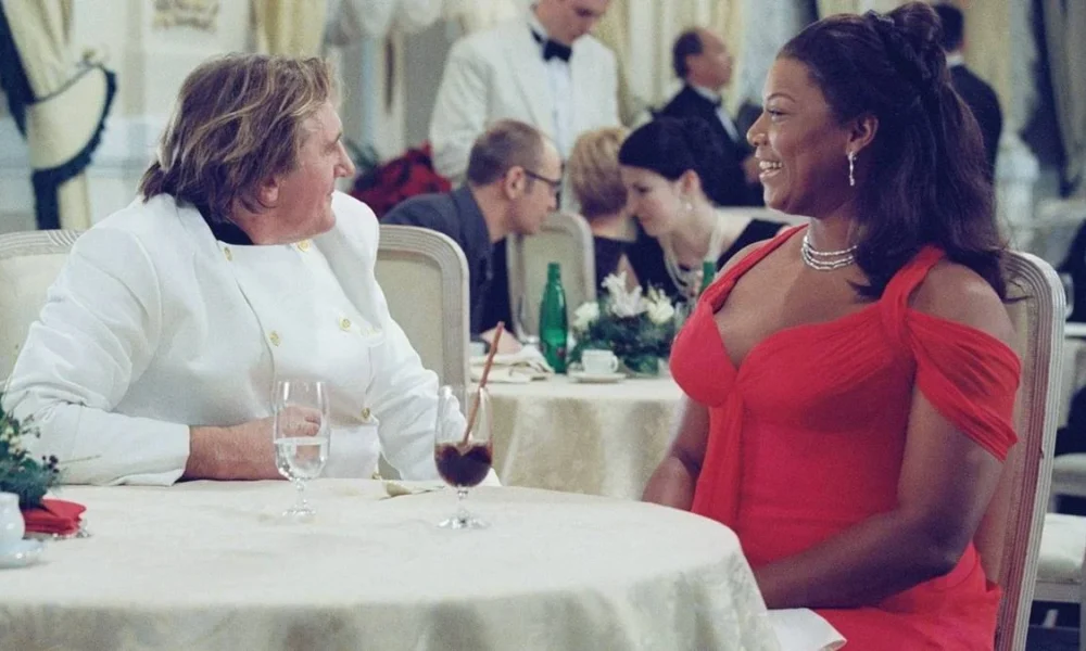 Queen Latifah sentada em uma mesa de gala em "As Férias da Minha Vida" (2006)