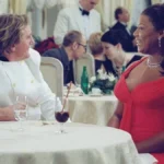 Queen Latifah sentada em uma mesa de gala em "As Férias da Minha Vida" (2006)