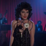 Isabella Rossellini como Dorothy Vallens, protagonista de Veludo Azul, performando uma música. Há pianistas atrás e um microfone em sua frente.