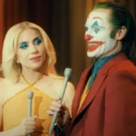 Lady Gaga e Joaquin Phoenix no filme "Coringa: Delírio a 2" (Joker 2) como os personagens Arlequina e Coringa. Ambos estão com maquiagem carregada e vestidos para um programa de televisão.