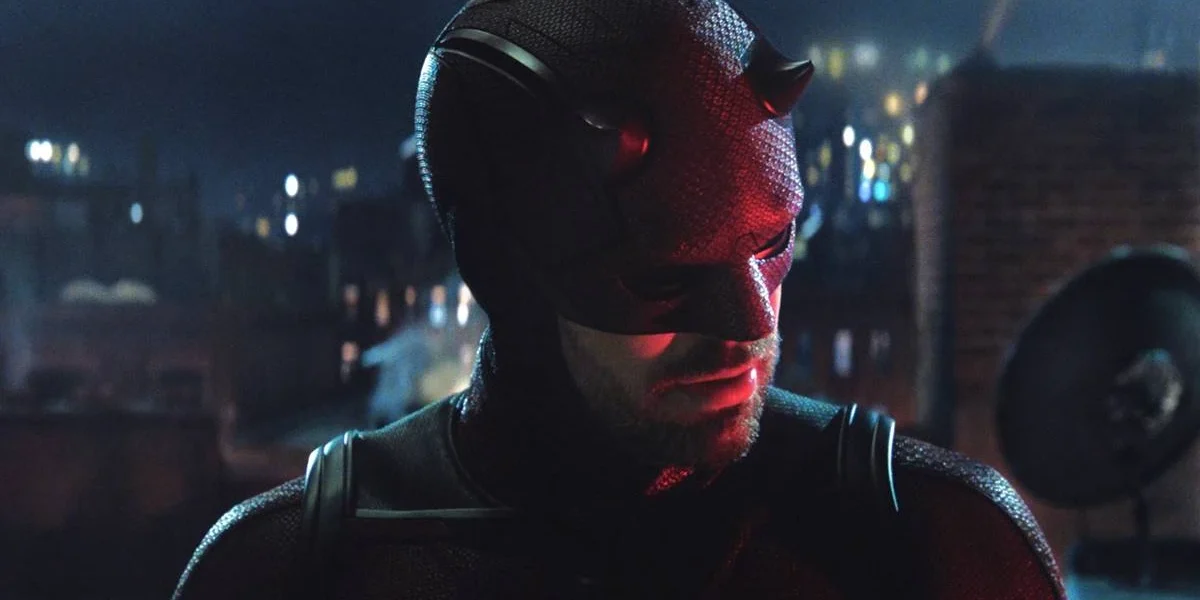 Charlie Cox como Matt Murdock, o Demolidor, em "Demolidor: Renascido". Personagem está uniformizado, focado pela câmera, e desvia o olhar olhando para baixo à direita.