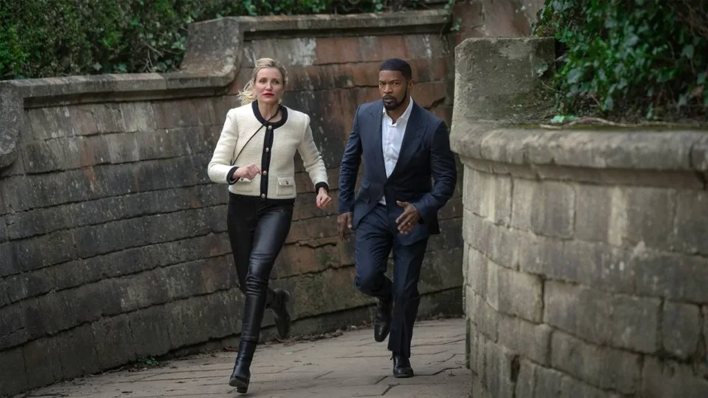 De Volta à Ação (2025) | Filme é Uma Checklist da Ação Genérica 1 Cameron Diaz, esquerda, e Jamie Foxx, direita, correndo em uma passagem de tijolos de pedra. Eles interpretam seus personagens de "De Volta à Ação" (Netflix, 2025).