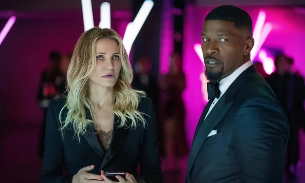 Cameron Diaz e Jamie Foxx, respectivamente à esquerda e direita, vestidos de trajes sociais, em um ambiente de fundo neon roxo, interpretando seus papéis em "De Volta À Ação" (2025).