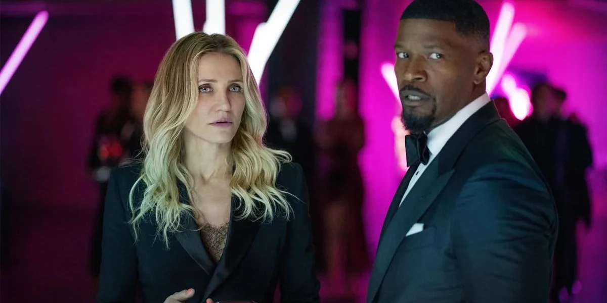 Cameron Diaz e Jamie Foxx, respectivamente à esquerda e direita, vestidos de trajes sociais, em um ambiente de fundo neon roxo, interpretando seus papéis em "De Volta À Ação" (2025).