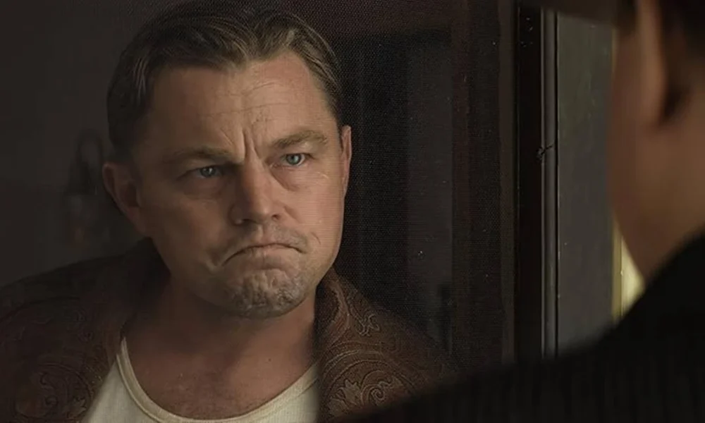 Leonardo DiCaprio interpretando Ernest Burkhart no longa "Assassinos da Lua das Flores" (ou "Killers of the Flower Moon" (2023). Ator está enquadrado em destaque à esquerda e olhando sério para outro personagem, de costas para nós.