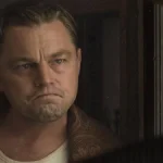 Leonardo DiCaprio interpretando Ernest Burkhart no longa "Assassinos da Lua das Flores" (ou "Killers of the Flower Moon" (2023). Ator está enquadrado em destaque à esquerda e olhando sério para outro personagem, de costas para nós.