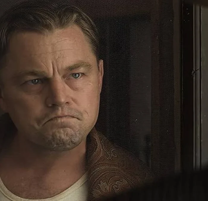 Leonardo DiCaprio interpretando Ernest Burkhart no longa "Assassinos da Lua das Flores" (ou "Killers of the Flower Moon" (2023). Ator está enquadrado em destaque à esquerda e olhando sério para outro personagem, de costas para nós.