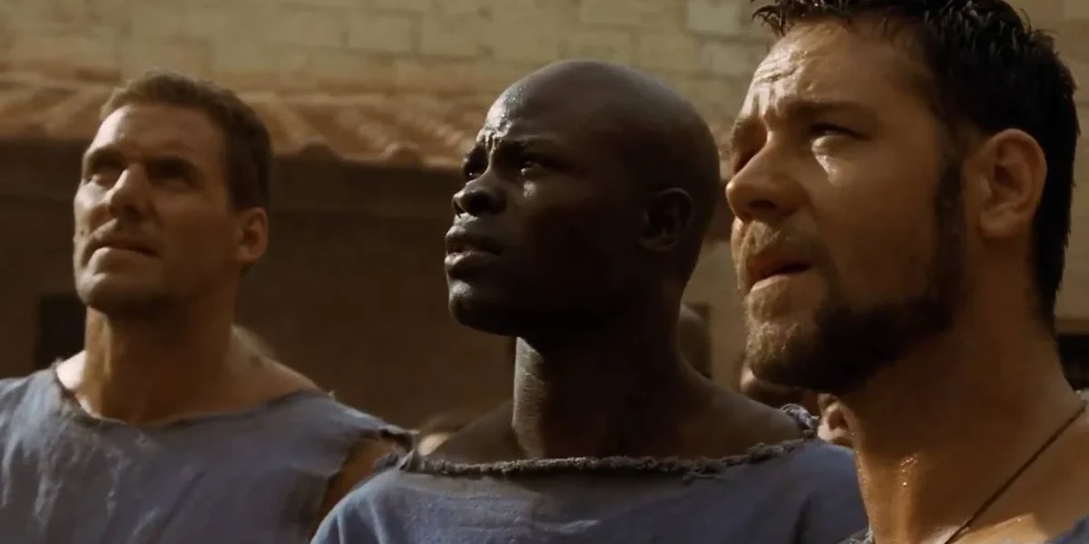 Ator DJimon Hounsou como visto em cena de "Gladiador" (2000), onde ele está ao centro, olhando longe da câmera, à esquerda da tela.