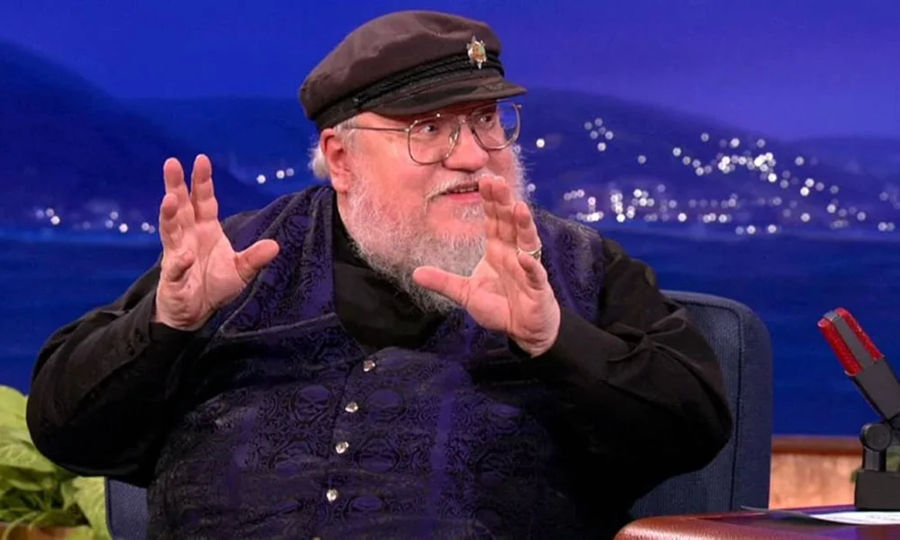 George R. R. Martin em entrevista, sorrind oe gesticulando.