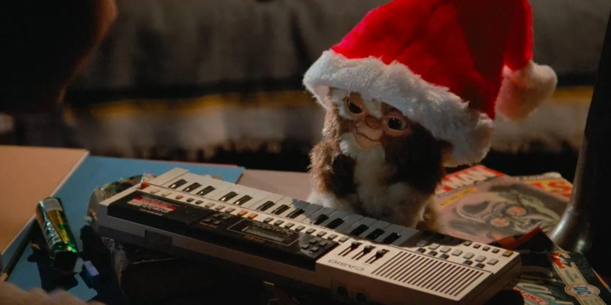 Estaria a Warner Brincando com Fogo ao Desenvolver Novos Filmes de “Gremlins” e “Os Goonies”, Sucessos dos Anos 80? Gremlin não monstrificado e com gorro de natal frente a um teclado. Imagem direta do filme "Gremlins" (1984).