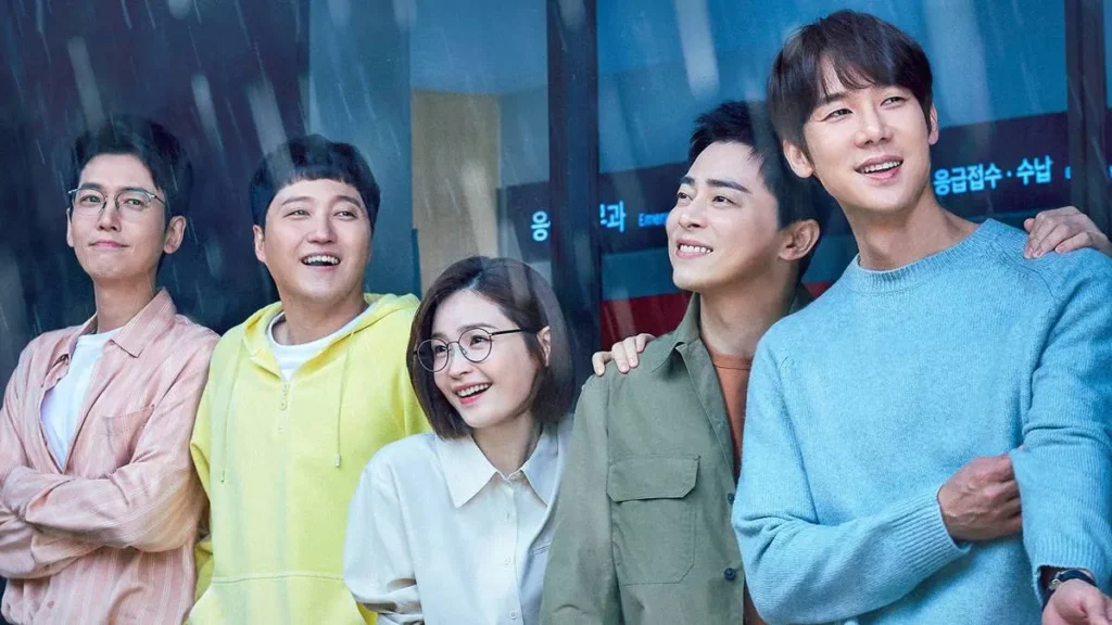 8 Doramas Para Assistir em Família 1 Os cinco protagonistas de "Hospital Playlist", disponível na Netflix, vendo a chuva cair por uma janela, vestidos com roupas casuais.