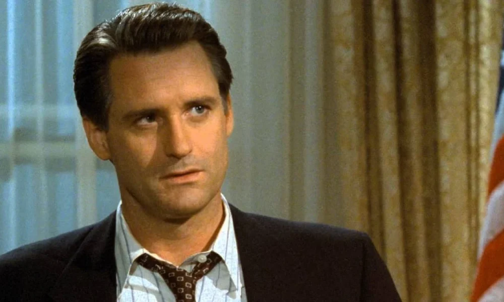 Bill Pullman como o presidente de Independence Day (1996). Há uma bandeira dos EUA ao seu fundo, à direita.