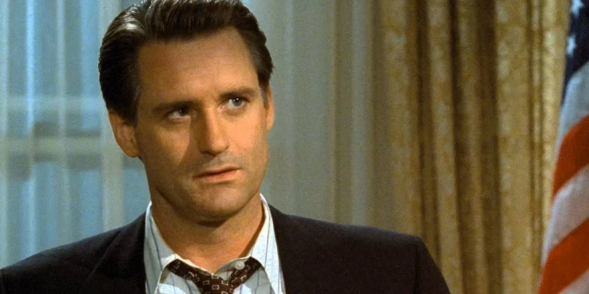 Bill Pullman como o presidente de Independence Day (1996). Há uma bandeira dos EUA ao seu fundo, à direita.