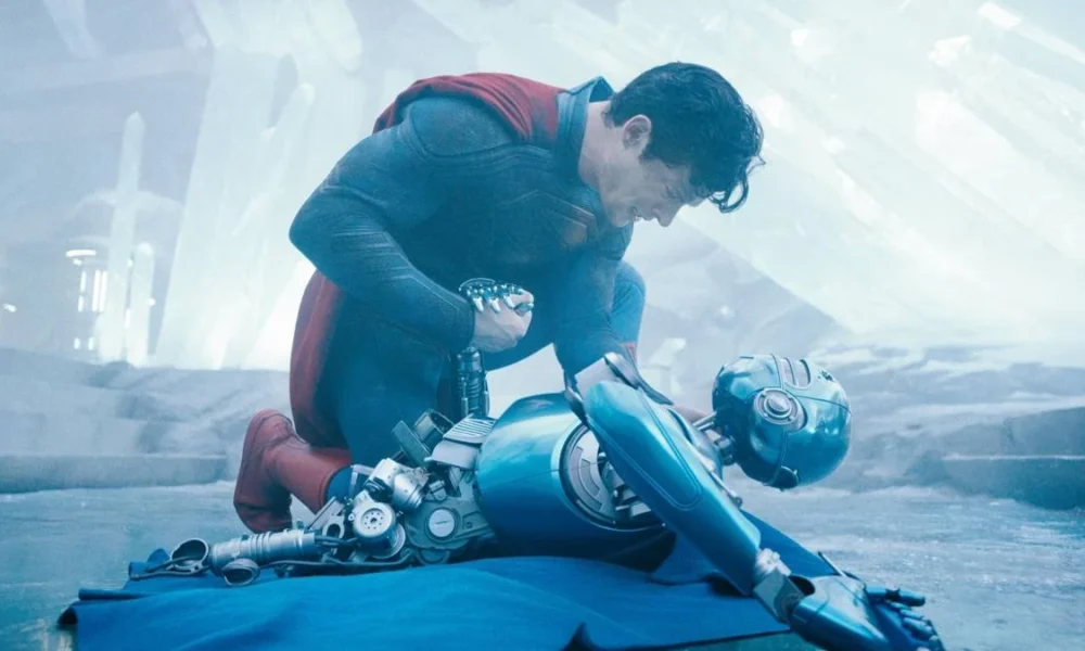 David Corenswet como o homem-de-aço, uniformizado, em "Superman" (2025), de James Gun. Ele está abaixado, agachado com pressão sobre um de seus joelhos, e olhando e lamentando a morte de um robô.