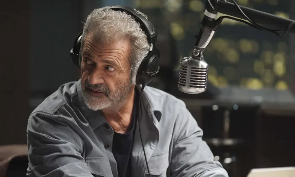 Donald Trump, em Mais Uma de Suas Maluquices, Elege Jon Voight, Mel Gibson e Sylvester Stallone  Seus “Embaixadores” em Hollywood a Partir de 2025 Mel Gibson em "On The Line" ou "Até o Limite" (2022), interpretando o protagonista radialista Elvis Cooney. Ele está na frente de um microfone, virando o roto para sua direita, como se ouvisse ou visse algo atrás de si.