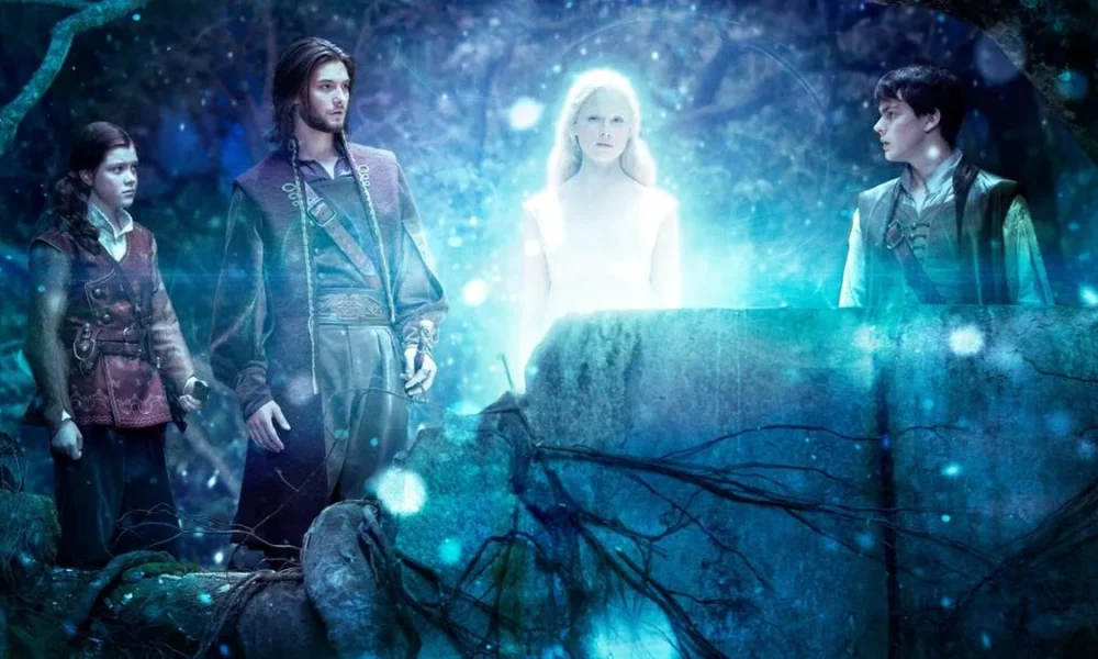 Georgie Henley (Lucy), Ben Barnes (Caspian), Laura Brent (Rainha de Nárnia), Skander Keynes (Edmund), da esquerda para a direita em "As Crônicas de Nárnia: Viagem do Peregrino da Alvorada" (2010). A Rainha de Nárnia brilha e todos olham para ela.
