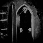Max Schreck em icônica cena de Nosferatu, com o vampiro Conde Orlok na porta.